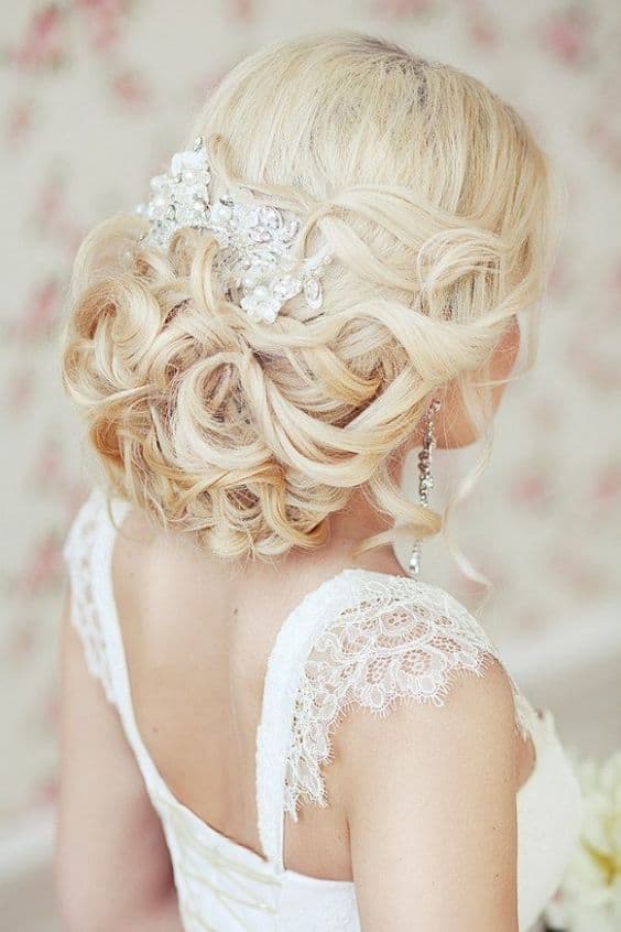 Back view of a romantic wedding updo featuring a soft low curly chignon adorned with a pearl-and-crystal comb, complemented by a lace gown.
