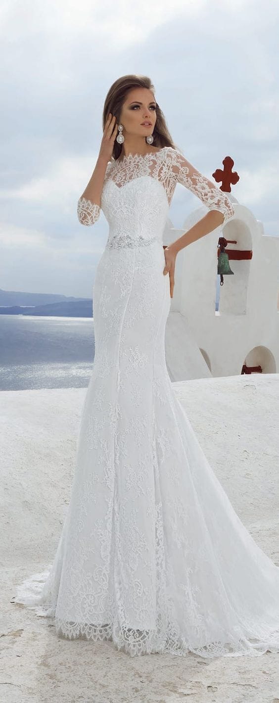 47 perfect bridal gown ideas - find yours 16 Elegant lace fit-and-flare bridal gown with illusion neckline and three-quarter sleeves, set against a coastal chapel backdrop.