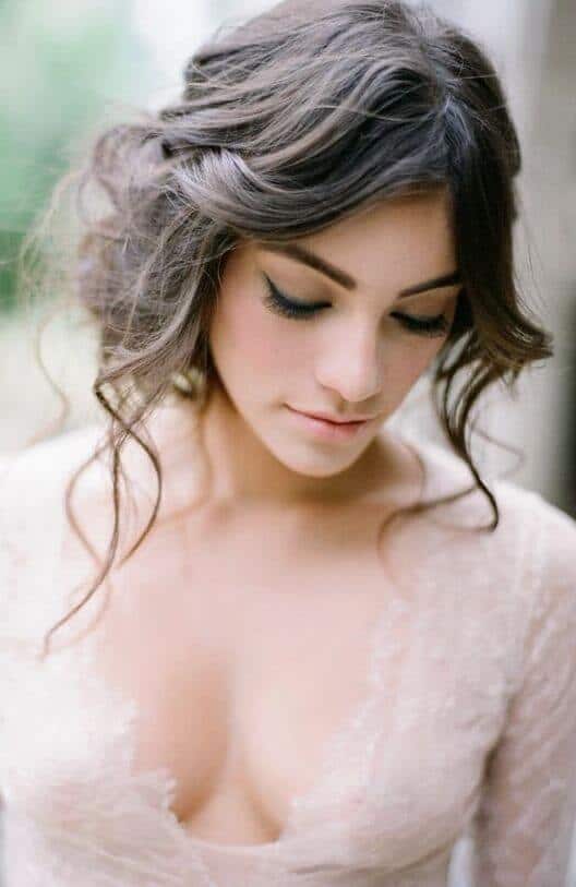 39 popular wedding hairstyles for brides to make your big day perfect 17 Soft bridal portrait showcasing wedding hairstyles for brides, featuring a loose updo with tendrils, lace v-neck gown, and natural makeup.