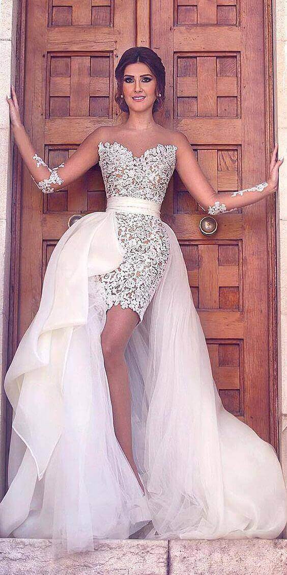 47 perfect bridal gown ideas - find yours 18 Bride in an ivory lace mini wedding dress with a detachable tulle overskirt and side bow, posing confidently in a grand wooden doorway.