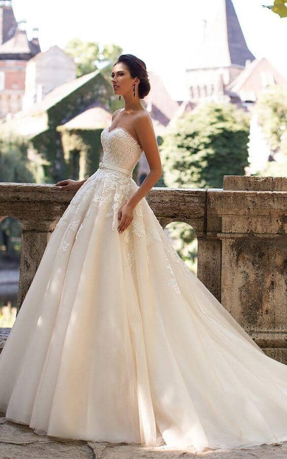 47 perfect bridal gown ideas - find yours 19 Bride in an ivory ball gown with a strapless sweetheart neckline, standing on a stone terrace overlooking a lush castle garden.