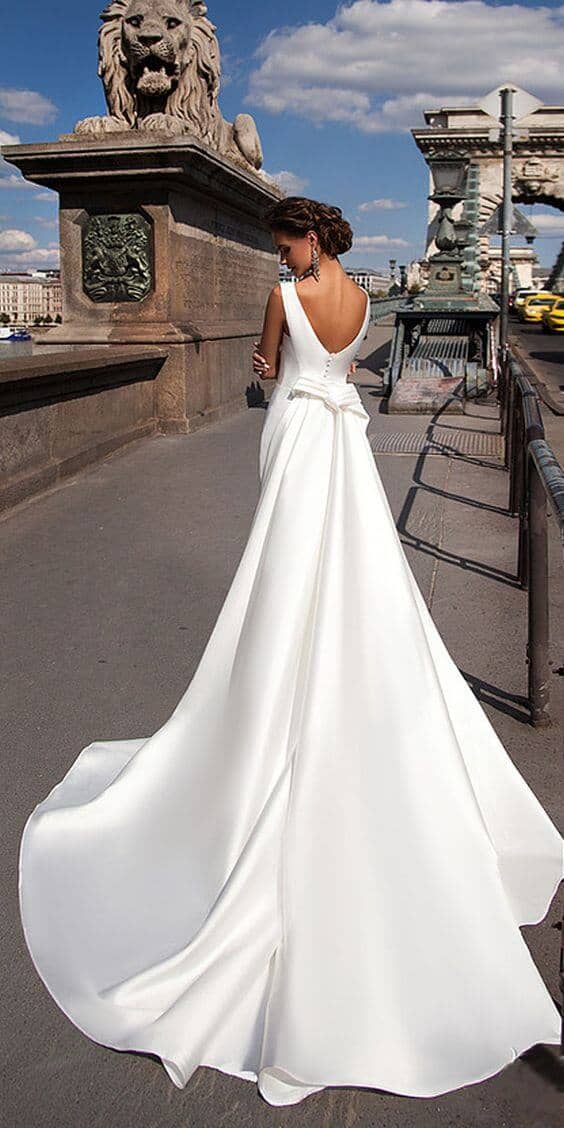 47 perfect bridal gown ideas - find yours 21 Bride in a minimalist ivory satin a-line ballgown with a chapel train, walking on a historic stone bridge beside a lion statue.