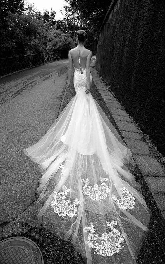 47 perfect bridal gown ideas - find yours 22 A bride in a fit-and-flare wedding gown walks along a hedge-lined lane, her cathedral-length tulle train flowing elegantly behind her.