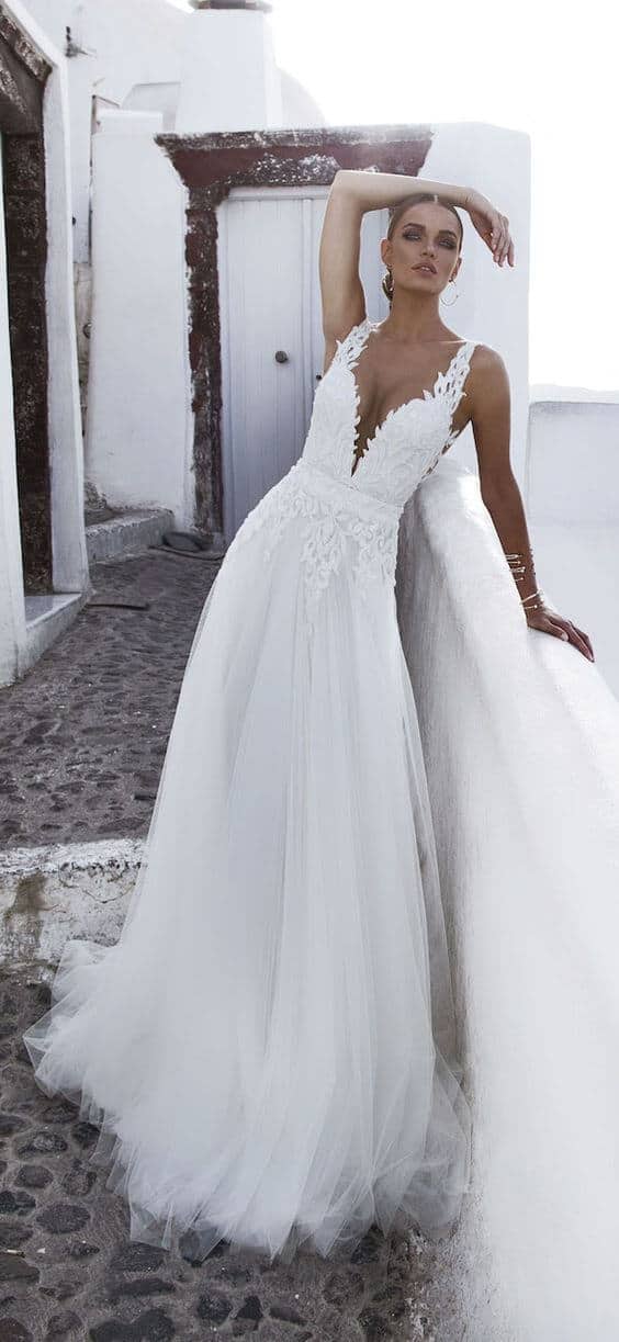 47 perfect bridal gown ideas - find yours 23 A bride in a whitewashed mediterranean alley wears an airy a-line tulle wedding dress with lace straps, leaning against a balustrade.