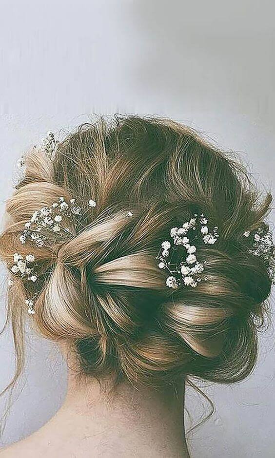 Romantic low twisted updo with blonde tones, adorned with delicate baby’s breath, perfect for weddings and bridal portraits.