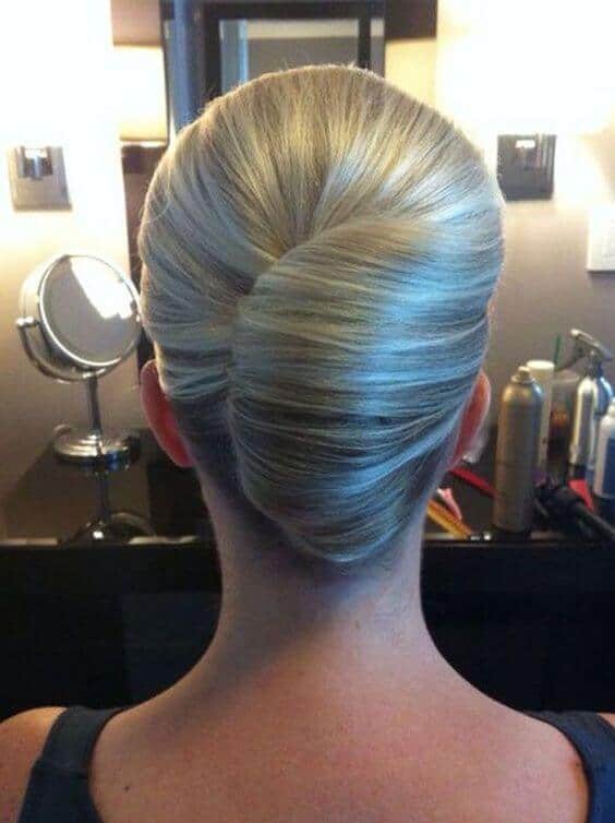 Sleek blonde french twist updo from the back, styled at a salon vanity with warm lighting and hair products, perfect for a wedding.