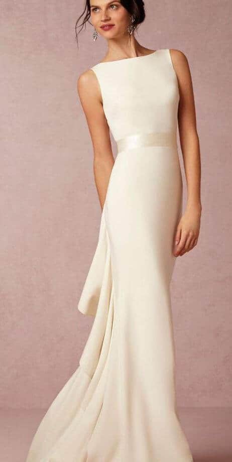 47 perfect bridal gown ideas - find yours 34 Minimalist ivory sheath wedding dress with bateau neckline, soft side drape, and subtle puddle train, set against a blush studio backdrop.