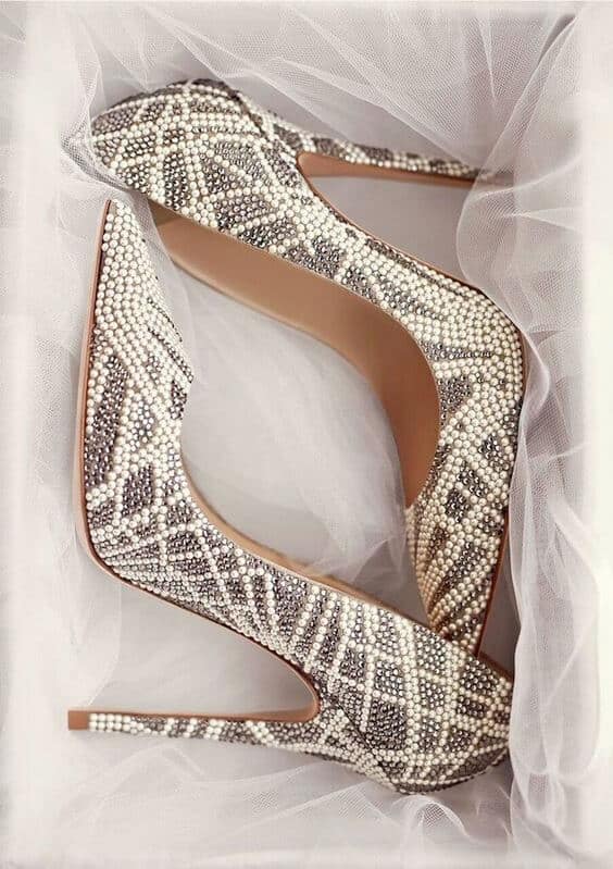 Glamorous wedding shoes high heels in a bridal box, encrusted with pearls and rhinestones, resting on soft white tulle.