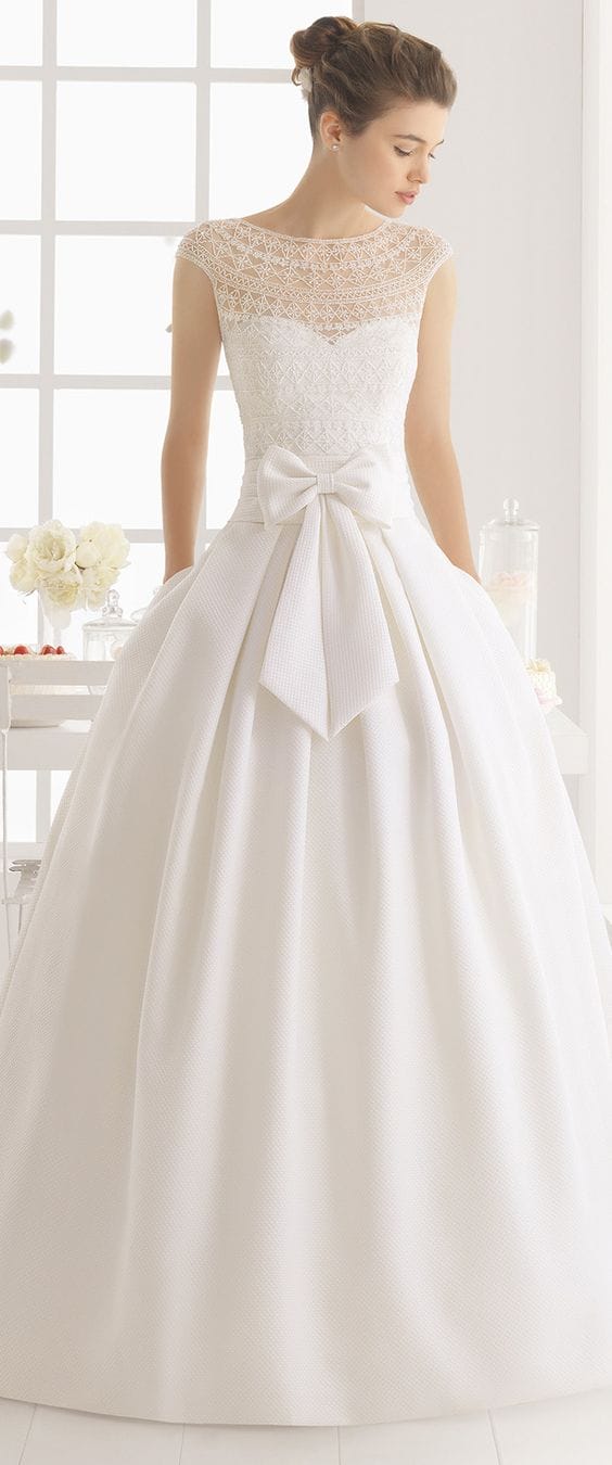 47 perfect bridal gown ideas - find yours 40 Classic ballgown with an illusion lace bodice and oversized bow, set in a bright studio with a minimalist dessert display and soft lighting.