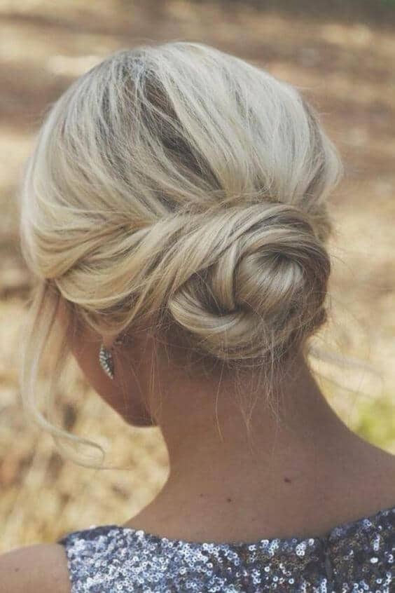 Romantic low chignon with airy volume, ash-blonde hair, and soft tendrils; perfect for a wedding at golden hour.