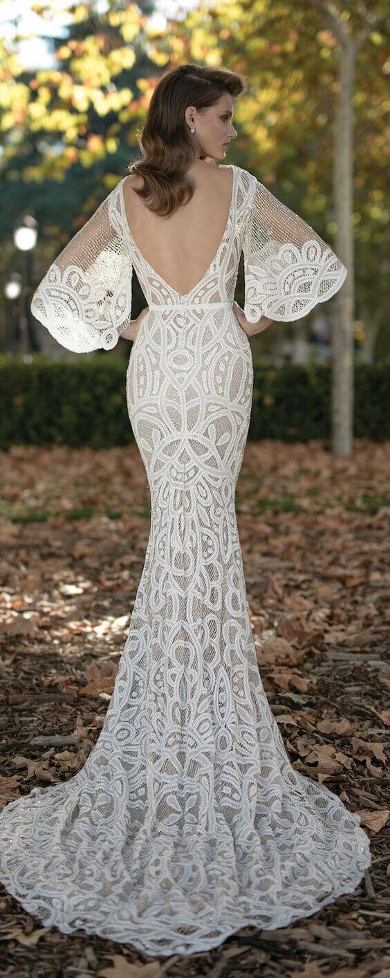 47 perfect bridal gown ideas - find yours 48 Back view of a bridal gown featuring geometric lace, a deep v back, and bishop sleeves, set in an autumn garden with golden light.