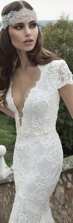 47 perfect bridal gown ideas - find yours 49 Bride in an ivory lace fit-and-flare gown with deep v neckline and cap sleeves, on a stone terrace surrounded by greenery.