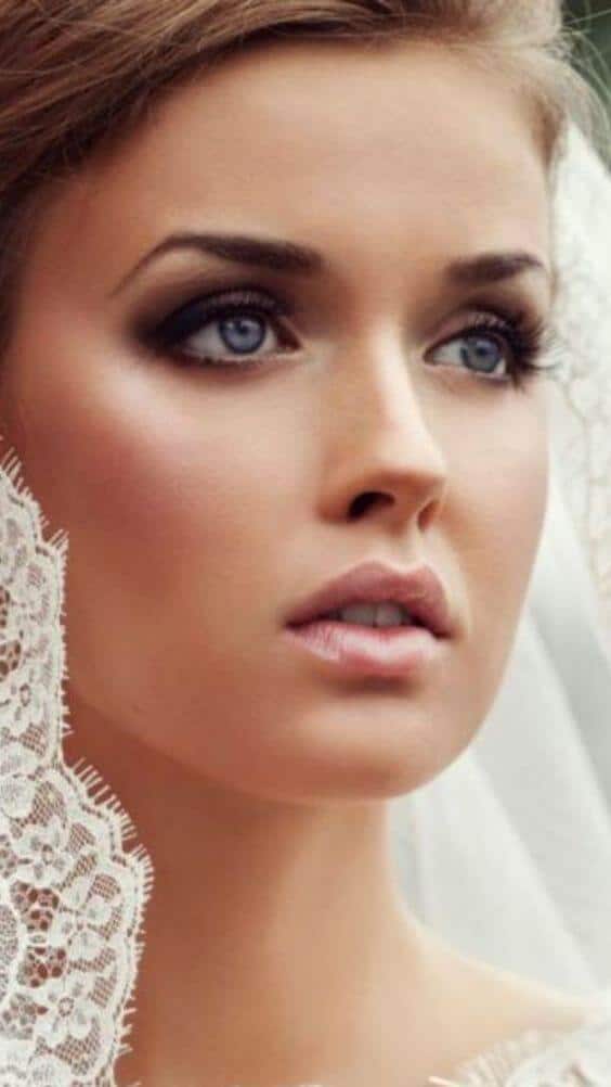 Close-up of a bride featuring elegant bridal makeup looks with an ivory lace veil, smoky taupe eyes, and soft peachy nude lips.