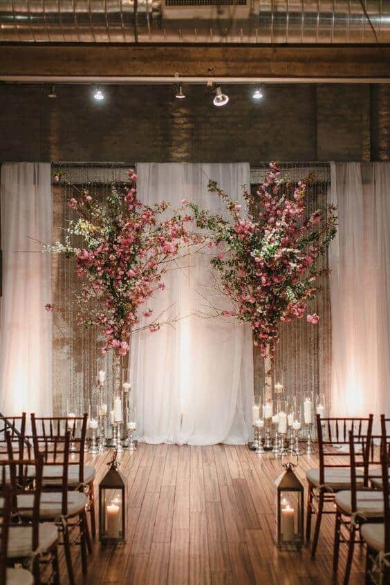 Candlelit loft wedding ceremony with pink flowering branches and a sheer white backdrop, creating an intimate, elegant atmosphere.