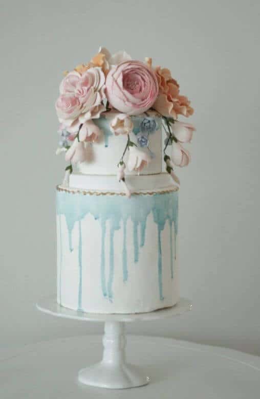 41 best wedding cake designs ideas for your big day 23 Pastel blue drip two-tier wedding cake on a white pedestal, adorned with cascading sugar florals and a gold beaded border.