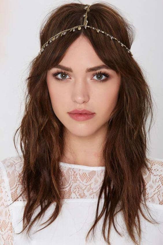 Close-up portrait of a model showcasing bridal makeup with soft taupe eyeshadow, muted rose lips, and a delicate gold head chain, embodying a boho bridal look.