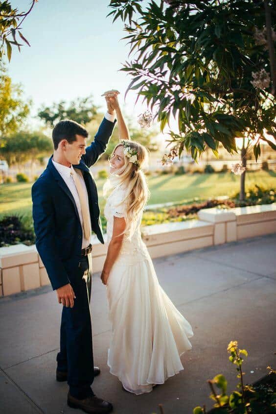 50 bride and groom photo ideas to save to posterity 33 Groom in a navy suit twirls the bride in a flowing white gown at golden hour, surrounded by a sunlit garden pathway.