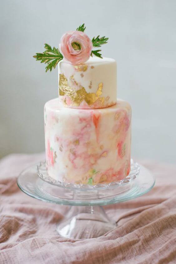 41 best wedding cake designs ideas for your big day 36 Two-tier wedding cake with watercolor buttercream in blush and ivory, adorned with gold leaf and a blush sugar ranunculus, on a glass pedestal.