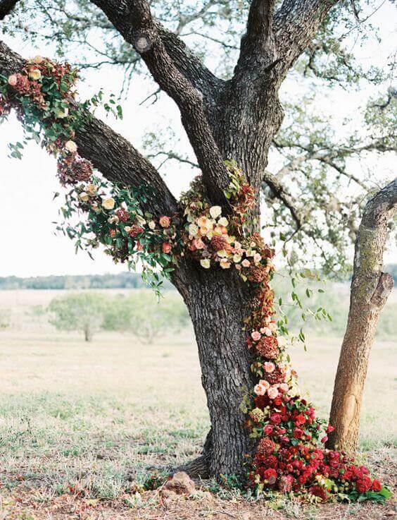 31 autumn wedding flowers ensembles perfect for your special day 12 Asymmetrical floral garland drapes a mature tree, featuring burgundy, blush, and cream blooms, creating a romantic autumn wedding backdrop.