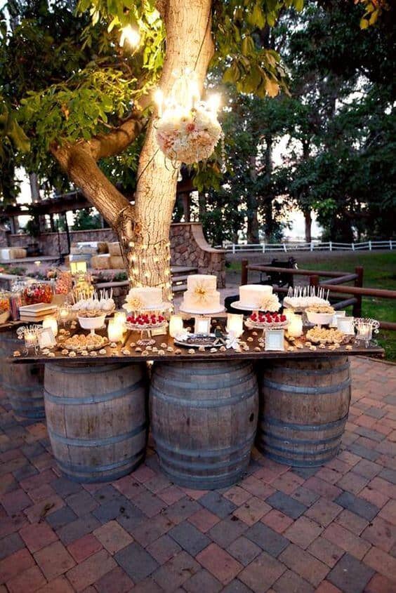 34 budget wedding ideas for a creative affordable wedding 14 Rustic outdoor dessert bar featuring three white tiered cakes, assorted sweets, and a floral chandelier under fairy lights, perfect for budget wedding ideas.