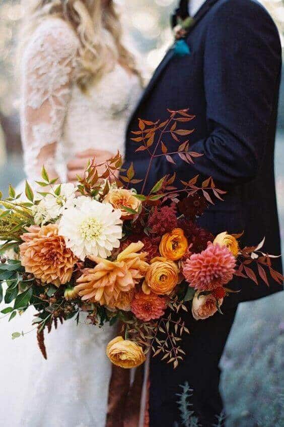 31 autumn wedding flowers ensembles perfect for your special day 15 Bridal couple portrait with a lush autumn wedding bouquet featuring dahlias, ranunculus, and garden roses in warm, earthy tones.