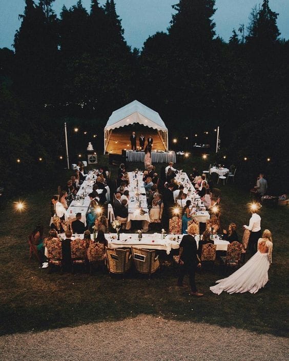 34 budget wedding ideas for a creative affordable wedding 16 Outdoor evening budget wedding reception with long banquet tables, warm bistro lights, and a small tented stage for speeches.