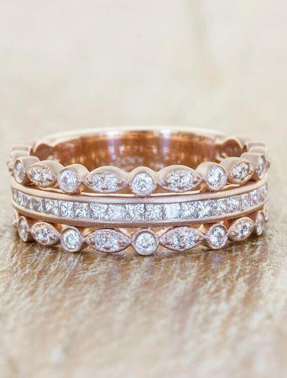 Stacked rose gold wedding bands featuring marquise bezels and channel-set princess cuts on a rustic wooden surface.
