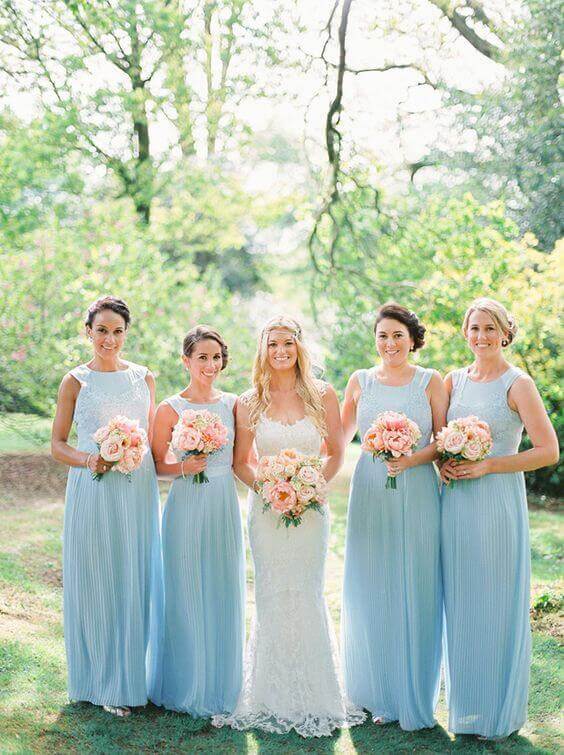 A romantic portrait of a bride and four bridesmaids in a sunlit garden. The bridesmaids wear floor-length ice-blue dresses, holding blush-peach bouquets.