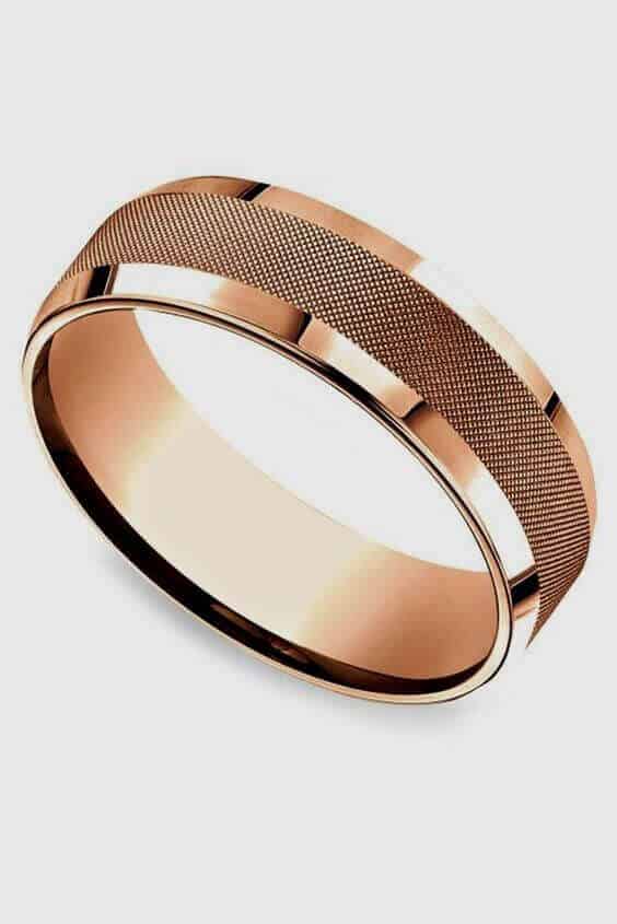 Rose gold wedding band featuring a knurled texture and polished edges, set against a light gray background.