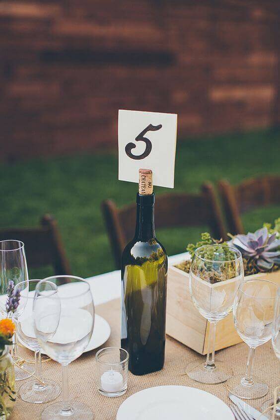 34 budget wedding ideas for a creative affordable wedding 20 Rustic outdoor wedding centerpiece featuring a green wine bottle as a table-number holder, set on a burlap runner with succulents.