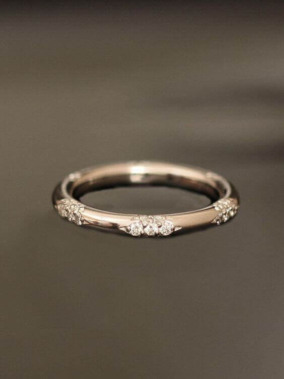 Slim white-gold or platinum wedding band featuring tiny round diamond clusters set around a polished surface, against a dark studio background.