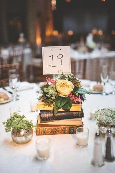 34 budget wedding ideas for a creative affordable wedding 21 Close-up of a round reception table featuring a stack of vintage books and a floral posy, evoking a romantic, budget-friendly wedding charm.