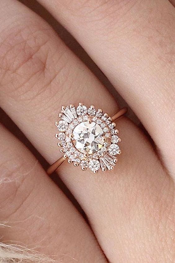 Rose-gold wedding band featuring a round brilliant center diamond and a starburst halo of round melee and tapered baguette diamonds.