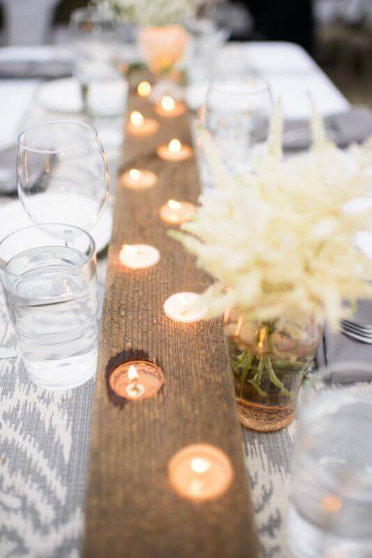 34 budget wedding ideas for a creative affordable wedding 23 Rustic wedding tablescape featuring a wooden candle runner, flickering tea lights, and soft blooms in mason jars, creating an intimate atmosphere.