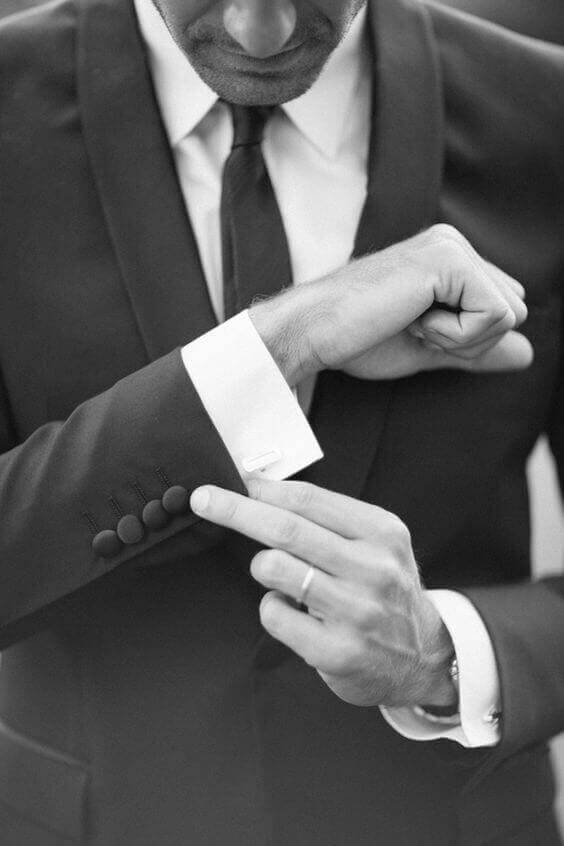 38 wedding accessories list - ideas to transform your big day into magic 25 Black-and-white close-up of a groom adjusting a cufflink on a crisp white french cuff, an elegant, timeless wedding accessories detail shot.