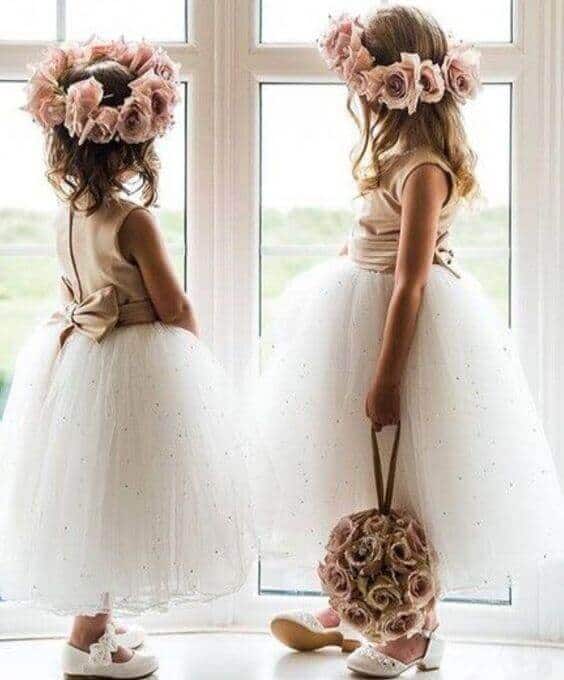 43 cute and perfect flower girl dresses that make every little princess shine 27 Two flower girls in blush satin dresses and ivory tulle skirts stand by a bright window; one holds a rose pomander.
