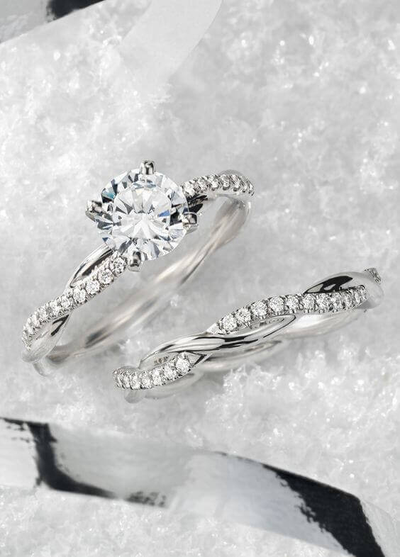Close-up of a twisted pavé diamond engagement ring paired with a matching wedding band, set on a snowy white background, showcasing wedding bands' elegance.