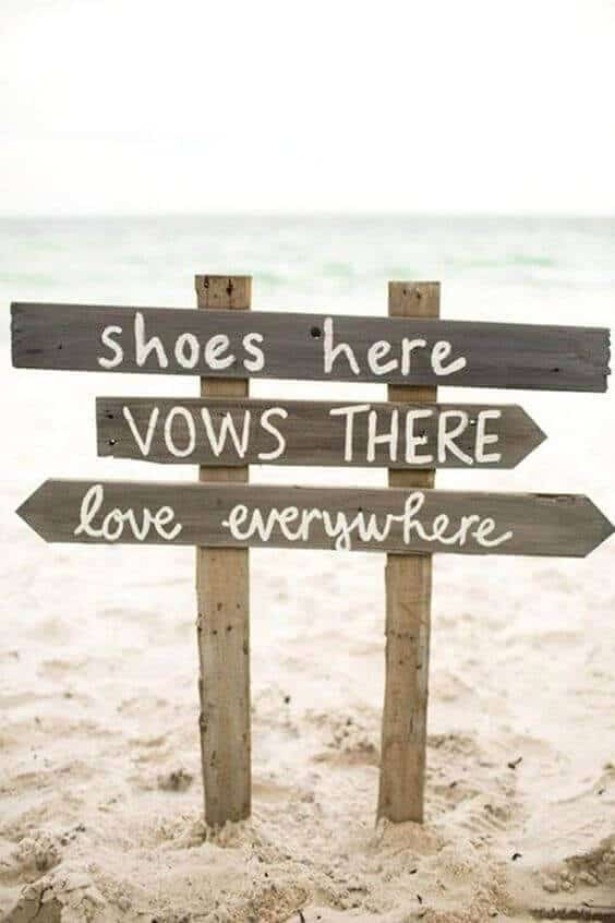 34 budget wedding ideas for a creative affordable wedding 28 Rustic wooden sign in soft sand directs guests at a budget-friendly beach wedding, promoting a relaxed, barefoot vibe.
