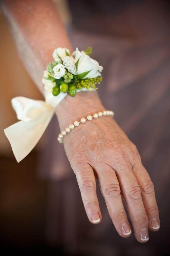 38 wedding accessories list - ideas to transform your big day into magic 28 Close-up of a feminine wrist adorned with an ivory floral corsage and classic pearl bracelet, set against a warm taupe background.