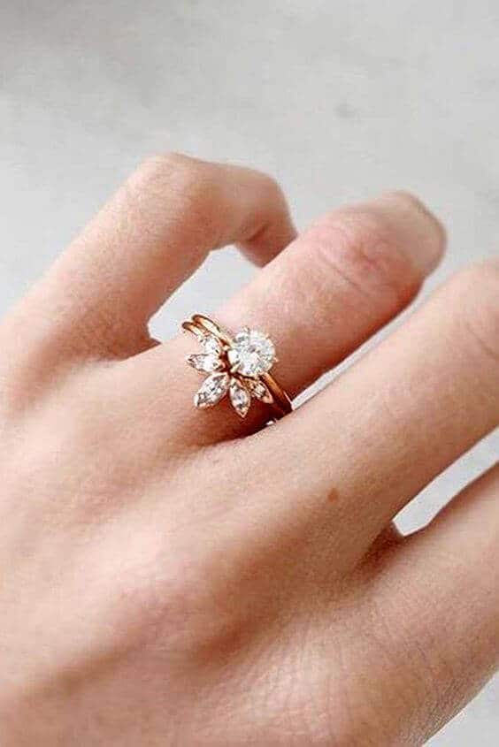 Close-up of a hand with a stacked wedding band and a round brilliant solitaire in rose gold, featuring a marquise diamond nesting band.