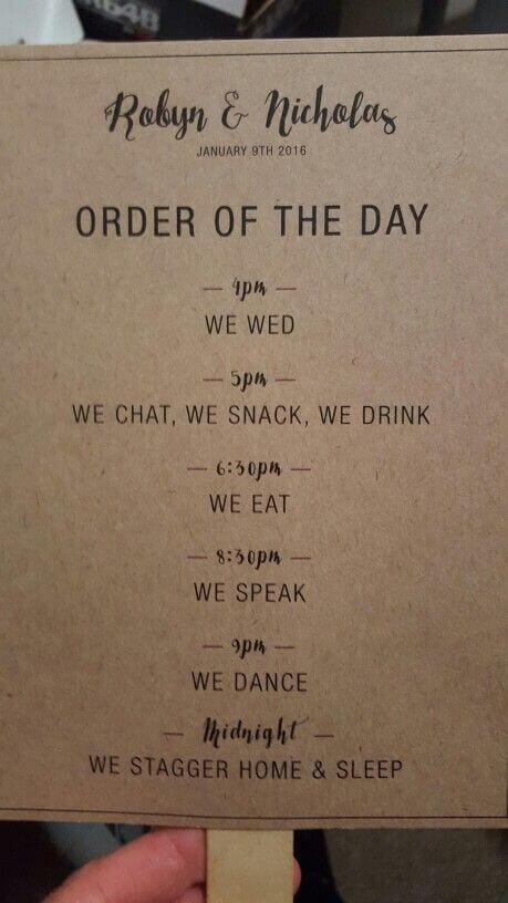 38 wedding accessories list - ideas to transform your big day into magic 31 Close-up of a rustic-chic wedding program paddle fan in kraft paper, featuring black typography and a wooden handle, held by a hand.