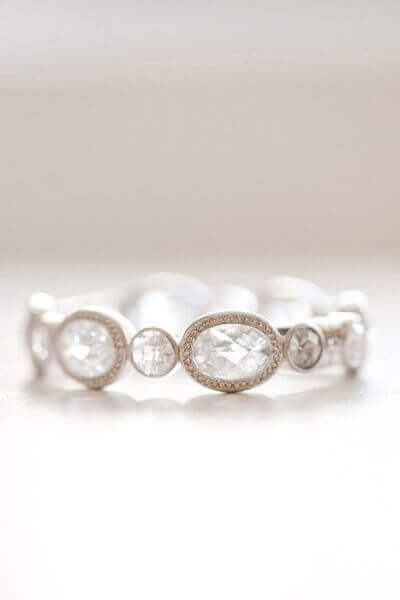 Elegant bridal bracelet featuring clear gemstones set in a white-metal band, resting on a soft ivory surface with a blurred background.