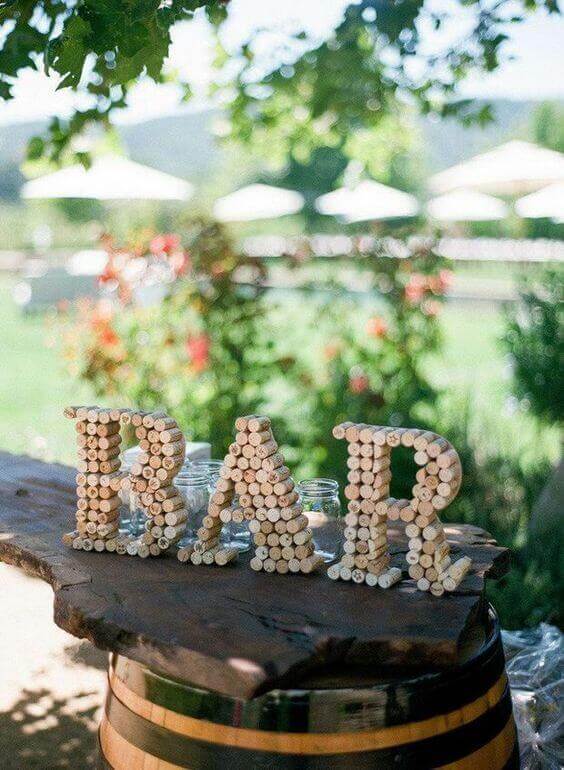 34 budget wedding ideas for a creative affordable wedding 5 Rustic wedding bar with "bar" made of wine corks on a live-edge slab atop an oak barrel, surrounded by a sunny garden.