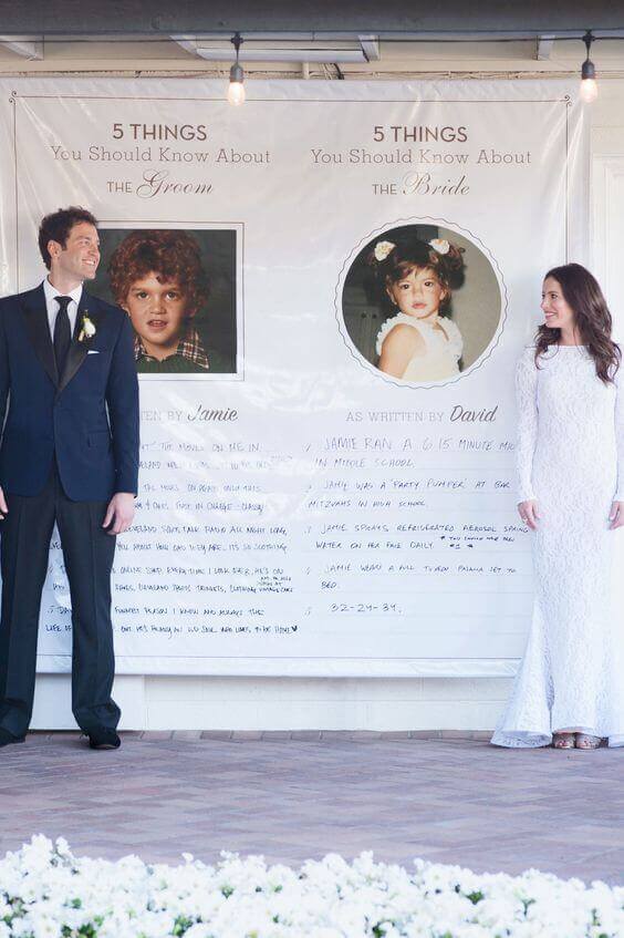 34 budget wedding ideas for a creative affordable wedding 32 Bride and groom stand beside a large white banner at their reception, showcasing childhood photos and fun facts, framed by white flowers and warm lights.