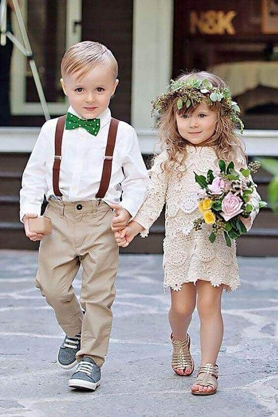 43 cute and perfect flower girl dresses that make every little princess shine 32 Flower girl in a cream crochet-lace dress, gold sandals, and floral crown, walking with a ring bearer in a white shirt and green bow tie.