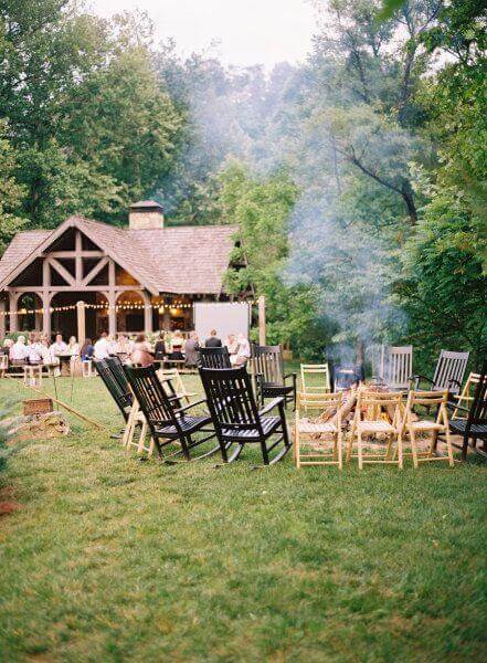 34 budget wedding ideas for a creative affordable wedding 33 Cozy rustic wedding reception with campfire, mismatched chairs, and twinkling bistro lights under a timber-frame pavilion.