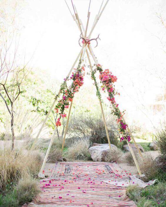 34 budget wedding ideas for a creative affordable wedding 35 A minimalist teepee-style wedding arch adorned with vibrant pink florals, set in a sunlit desert garden for an intimate budget wedding.