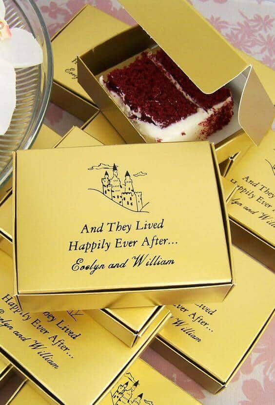 38 wedding accessories list - ideas to transform your big day into magic 36 Stacked gold wedding favor boxes featuring a castle illustration and the phrase 'and they lived happily ever after... ' with one box revealing a red velvet cake slice.