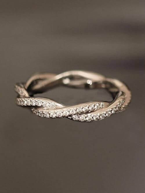 Twisted wedding band featuring micro-pavé diamonds entwined with a polished white metal strand, set against a dark background.