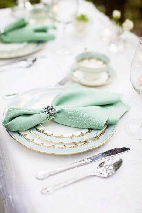 38 wedding accessories list - ideas to transform your big day into magic 38 Elegant wedding tablescape featuring mint napkin, vintage gold-rimmed china, silver flatware, and crystal stemware, set outdoors.
